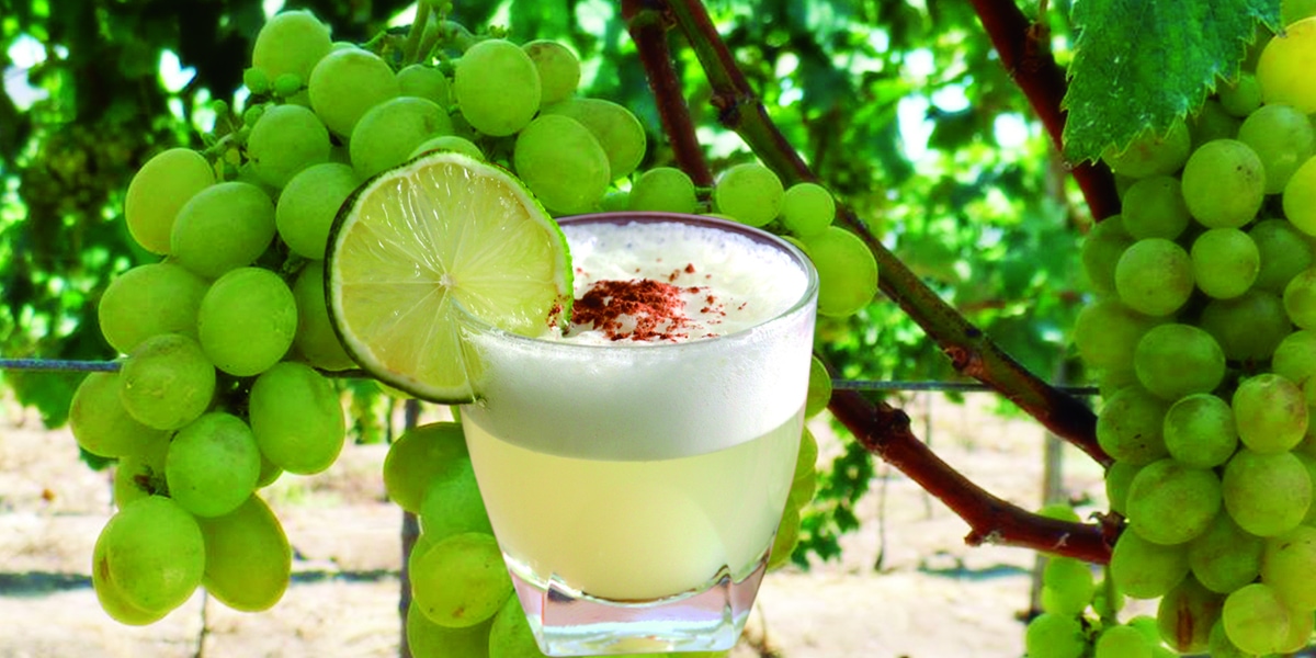 vaso de pisco sour con fondo de uvas verdes